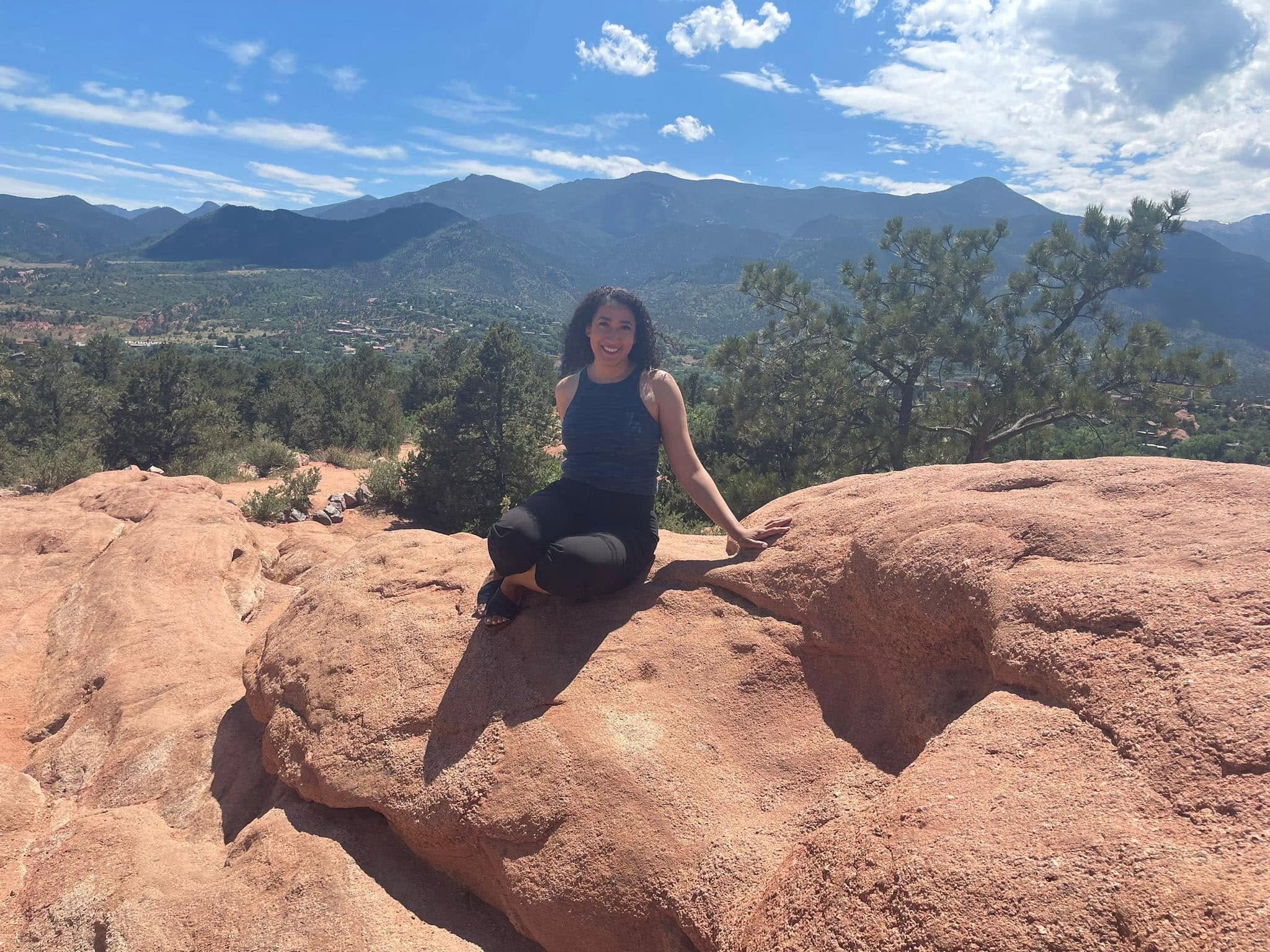 Katherine Fernandez sitting on red sandstone at Garden of the Gods, with the Front Range behind her